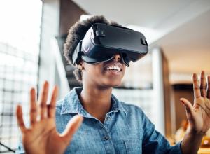 Smiling african-american woman wearing virtual reality headset in office. Young female at startup using VR goggles.