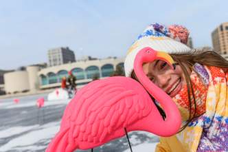 A young girl peaks through a plastic pink flamingo while standing on a frozen Lake Monona.