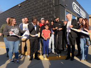 A group of community members and local leaders stand outside a business during a ribbon-cutting ceremony, smiling and holding oversized scissors as they celebrate a grand opening.