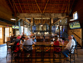 Guests gather around the bar inside Milwaukee Brewing Company, where exposed timber beams, stainless steel brewing tanks and warm industrial architecture create a lively taproom atmosphere.