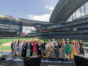 Group photo of attendees at Visit Milwaukee's Annual Meeting, posed on a stage at American Family Field (Milwaukee Brewers stadium) with stadium seating and banners visible in the background.