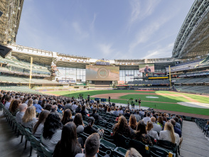 Crowd of business attendees seated in American Family Field's lower bowl during the Visit Milwaukee annual meeting, with the baseball stadium's retractable roof open and a presentation screen visible on the outfield wall.