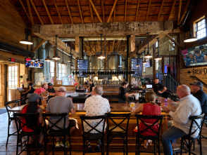 Guests gather around the bar inside Milwaukee Brewing Company, where exposed timber beams, stainless steel brewing tanks and warm industrial architecture create a lively taproom atmosphere.