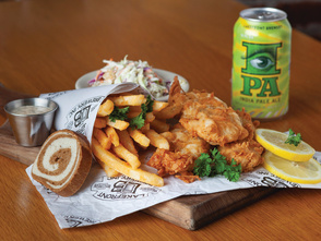 A painted figure sitting on a crescent moon hangs from the arched brick ceiling inside the Miller Caves.
A fish fry with fried cod, fries, coleslaw, rye bread, lemon slices and a can of IPA served on a wooden board.