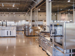Spacious showroom with rows of commercial kitchen equipment, including stainless steel refrigerators, ovens, and workstations.