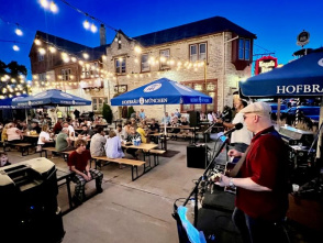 A wide, nighttime view of the Kegel's Inn patio, with string lights illuminating the space, as musicians play their instruments in the foreground and diners enjoy food and drinks in the background.