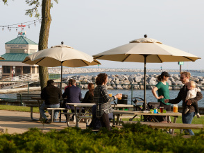 A group of people enjoying beers under umbrellas at the picnic tables outside of the Roundhouse Beer Garden in Milwaukee along the Lakefront.