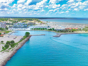 An aerial view of Reefpoint Marina along the Lake Michigan shoreline, featuring rows of docked boats, a protected harbor, and vibrant blue water. Waterfront buildings, green spaces, and a lakeside cityscape stretch beneath a sky filled with scattered clouds.