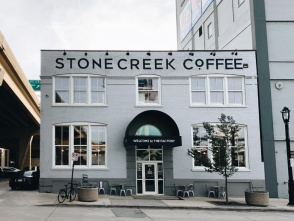 Exterior of Stone Creek Coffee’s white brick building with large front windows, black awning, and outdoor seating along the sidewalk.