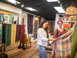 Two women examining a colorful woven textile in a bright fabric at Cultural Cloth.