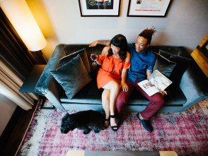 a couple sitting on a couch reading a magazine with a dog at their feet