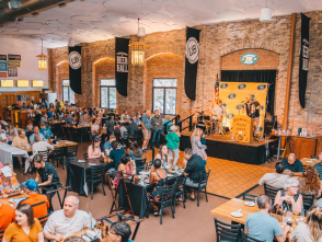 An open banquet hall filled with people eating food and drinking beer while a performer plays the accordion in the background.