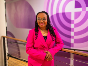 LaShawndra Vernon stands with hands clasped in front of a larger purple mural