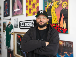 headshot of a latino man with a beard smirking in front of a colorful gallery wall with a ball cap on and his arms crossed