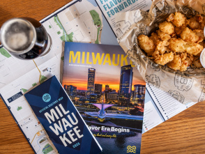 The 2026 Milwaukee Official Visitors Guide and Official Visitors Map are displayed with a beer and cheese curds on a table.