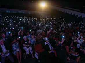 a large crowd using their cell phone flashlights in a dark auditorium