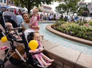 A family with a stroller and balloons in front of the fountain on the Bentonville square.