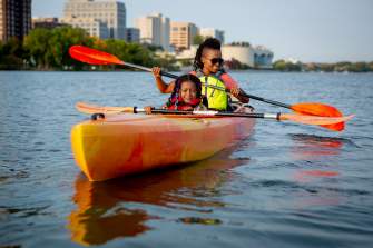 A Black woman and young Black girl kayak on Lake Mendota with the Madison skyline in the background