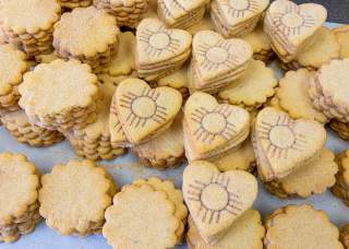 Piles of biscochito cookies, some with a traditional rounded shape and some in a heart shape branded with a Zia symbol.