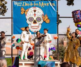Mariachi Performers and singer on stage in front of Dia de los Muertos banner for the annual event