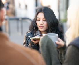 Young_Woman_Holding_Phone_While_Socializing_Outdoors_with_Friends