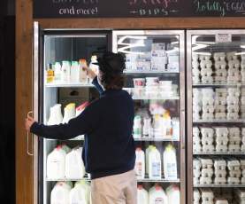 Shopper selecting a bottle from a refrigerator stocked with local milk, dairy products and eggs at Don-O-Ray Farm Market in Kelowna.