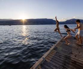 Friends jumping off the dock into Okanagan Lake at sunset in City Park