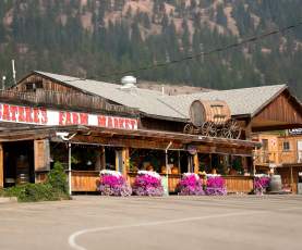 Exterior of Gatzke’s Farm Market in Lake Country, with rustic wooden buildings, colourful flower baskets and a barrel wagon against a forested hillside.