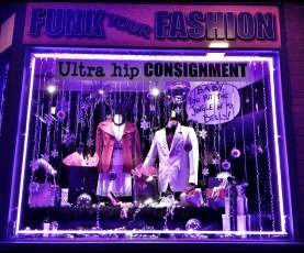 The Funk Your Fashion consignment store window glows with purple lighting, displaying two mannequins in colourful jackets surrounded by hanging ornaments, snowflakes, and holiday decorations.