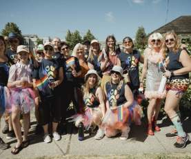 A group of people dressed in rainbow skirts and black shirts with a rainbow paw print, smiling at the camera.