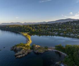 Aerial view of a narrow shoreline separating ocean and lagoon with forest and homes beyond.