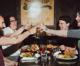 Four people at a restaurant table raising glasses in a toast over food.