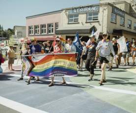 A group of people marching on the street with a pride flag.