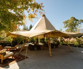 An image of a tipi setup for a dinner event outside with trees and sunny sky