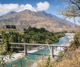 Tall trail bridge over blue river stream with mountains in background