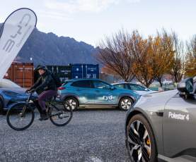 Electric cars out for display with the Remarkable Mountain range in the background and a person on an electric bike riding through the frame