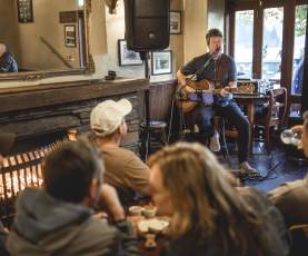 Musician playing guitar to people at Pog Mahones Irish Pub