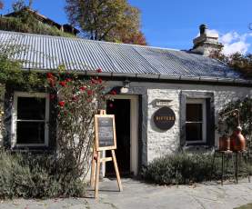 The outside of a white brick cottage with signs out the front for gin tasting