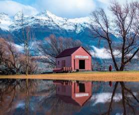 Red wharf shed and snowy mountains reflecting on the river
