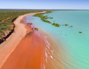Aerial view of Roebuck Bay Broome showing the turquoise waters and pindan red stained sands, with a flock of birds resting on the beach