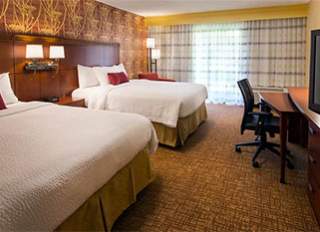 Courtyard by Marriott San Bruno Double Queen Bedroom. Two beds with white bedding and a desk with a chair in a hotel room.
