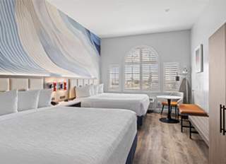 Hotel Skye SFO Double Queen Bedroom. Beds with white bedding in a well-lit room with wood-paneled flooring.