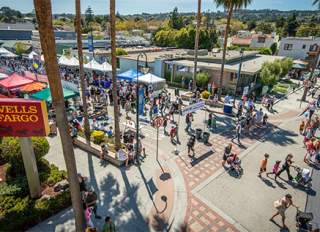 Millbrae Art and Wine Festival. People walking around festival. Palm trees and Wells Fargo sign in background.