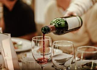 Red wine from a green bottle being poured into a clear wine glass