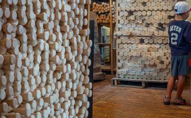 Image of a young baseball fan in a room with raw bats stacked in a storage room.