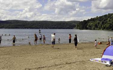 Groups of people on a sandy beach with a lake and hills in the background.