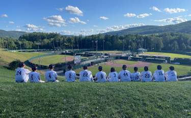 A youth baseball team sitting on a hill overlooking baseball fields