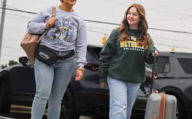 Two travelers smiling as they cross a street with luggage on their way to a hotel in Cumberland County, North Carolina.