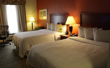 Cozy hotel room in Fayetteville, North Carolina with two neatly made double beds, soft lighting, and a comfortable seating area.