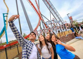 A group of four people posing for a selfie in front of a roller coaster that reads Iron Menace